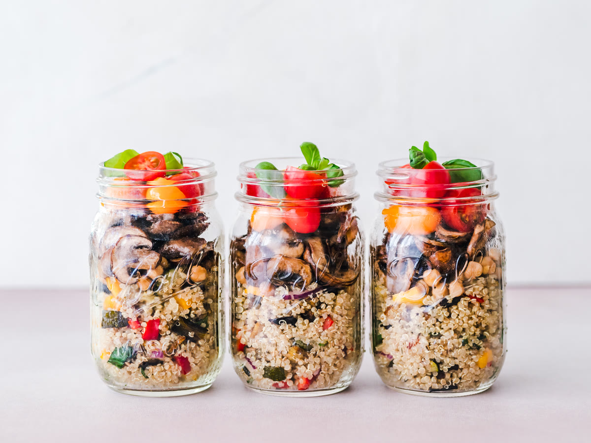Tres frascos de vidrio con comida preparada por adelantado, con verduras y jitomate encima