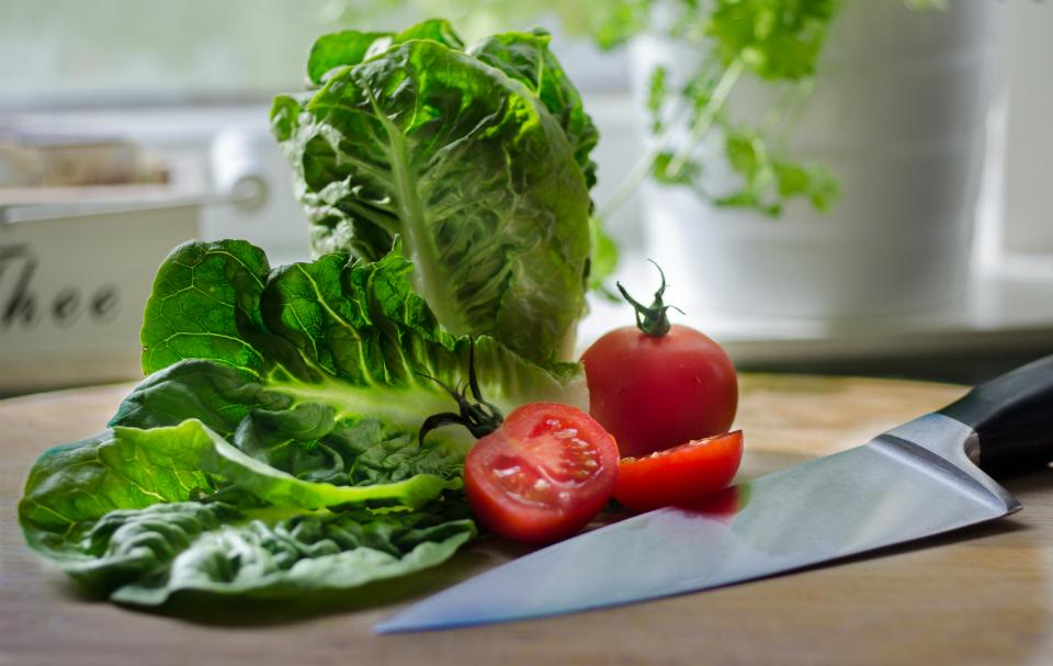 Hojas de lechuga orejona y jitomates recién lavados sobre una tabla, junto a un cuchillo